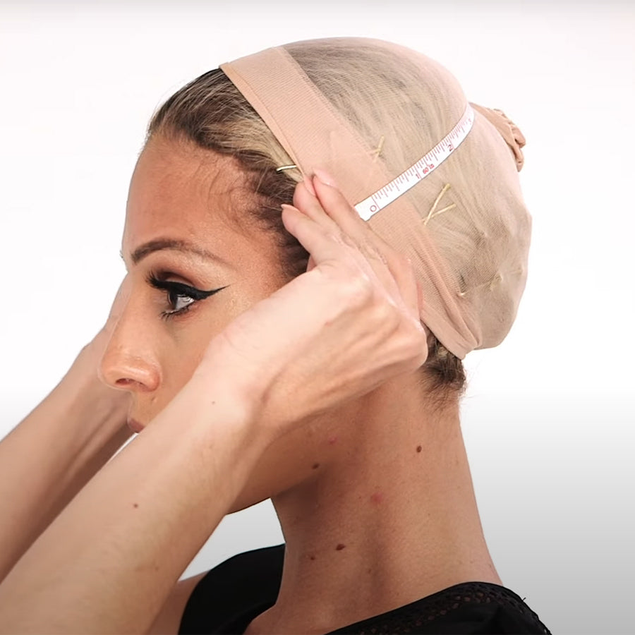 Woman wearing a wig cap measuring her head with a measuring tape.